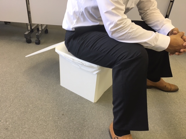 成人の男性が試しに座ってみても頑丈なつくりとなっている組み立て後の簡易トイレの写真