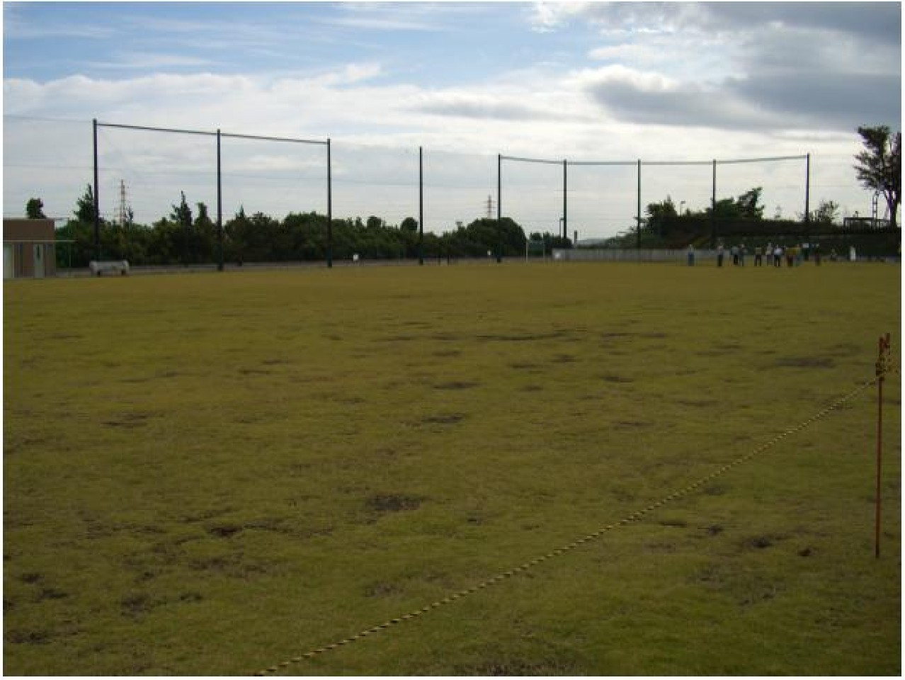大きな防球フェンスが奥側一面に貼られている芝生の多目的広場の写真