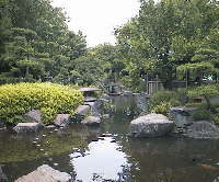 周りにたくさんの木々や屋根付きのベンチなどがある石垣に囲まれたたちばなの池の写真
