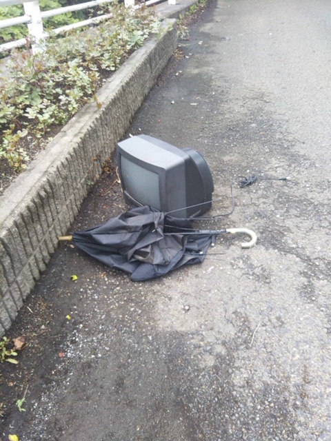 道路の脇に捨てられた壊れたテレビと傘の写真