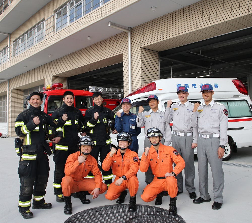 オレンジ色の活動服を着ている救助隊員（レスキュー）、黒色の防火衣を着ている消防士、グレーと紺色の活動服を着ている救急救命士が笑顔でこぶしを握ってガッツポースをしている写真