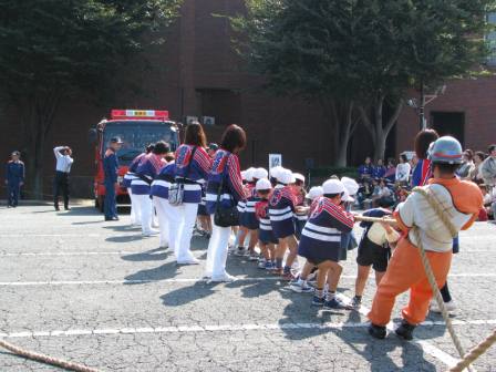 法被を着た子ども達が消防車と繋いだ綱を引っぱって、綱引きをしている写真