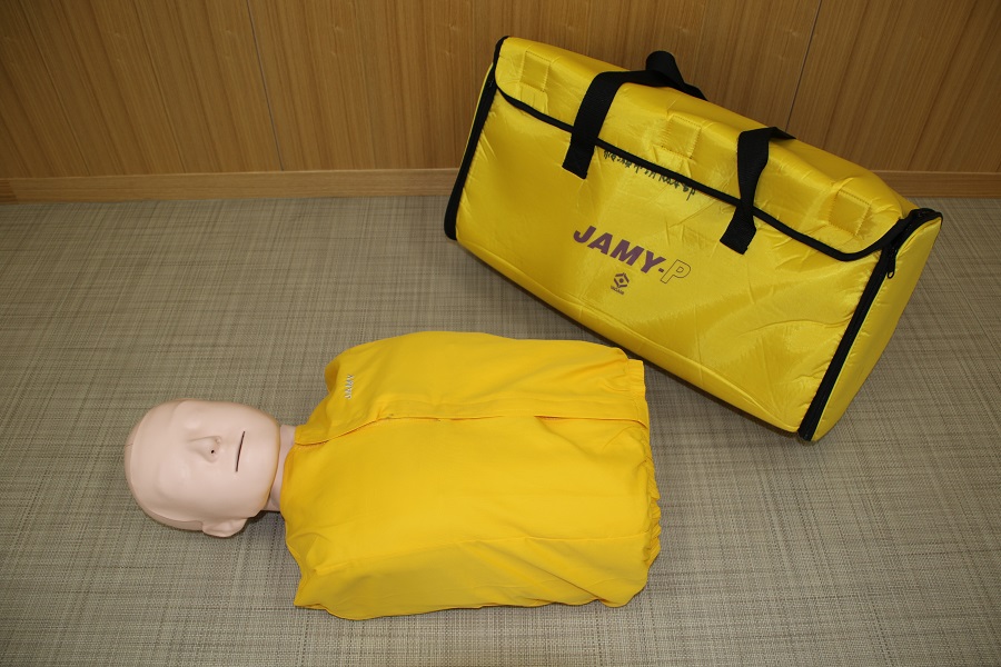 黄色の服を着た上半身（腕なし）タイプの成人心肺蘇生訓練用人形と黄色のソフトケースの写真