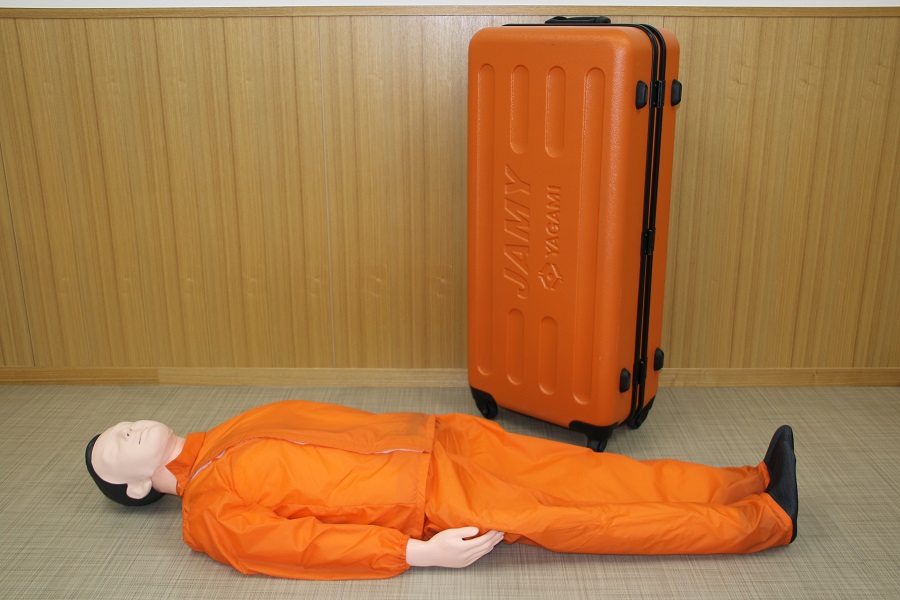 オレンジ色の服を着た全身タイプの成人心肺蘇生訓練用人形とオレンジ色のキャスター付きハードケースの写真
