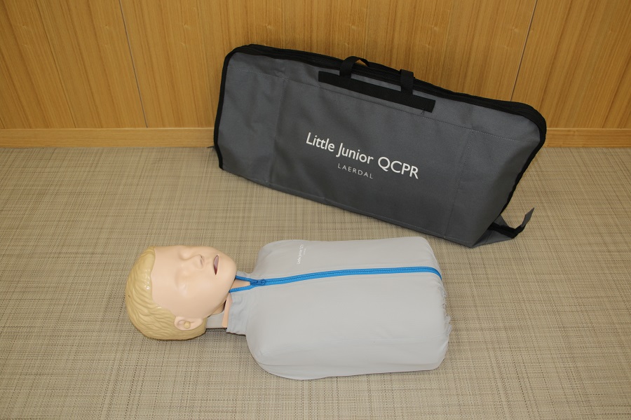 ライトグレーの服を着た上半身（腕なし）タイプの小児心肺蘇生訓練用人形と灰色のソフトケースの写真