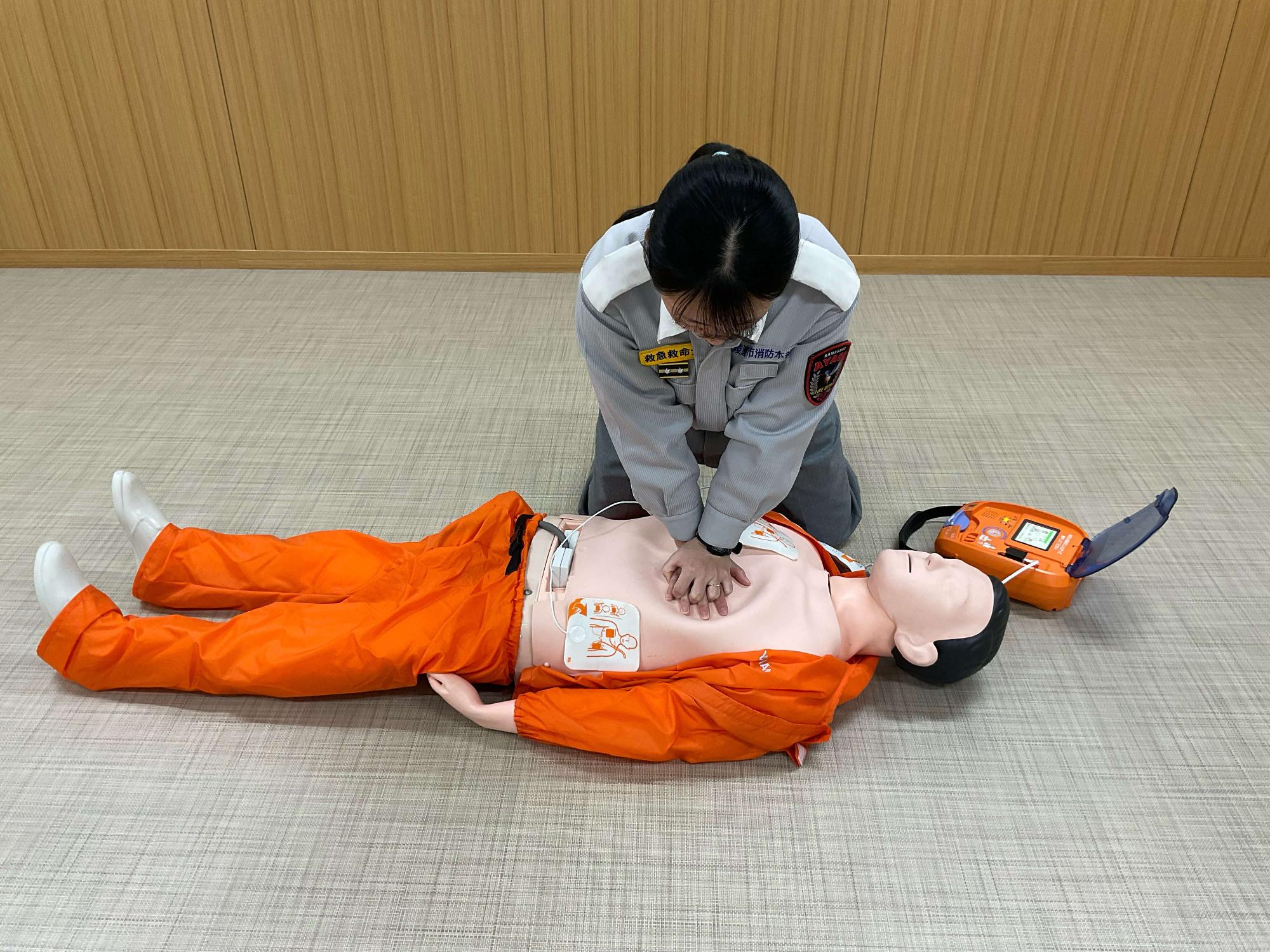 AEDのパッドが貼られた状態で胸骨圧迫を行っている写真