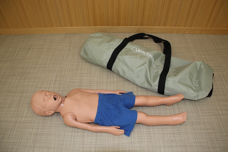 青色のズボンを履いた全身タイプの小児心肺蘇生訓練用人形とミントグレーのソフトケースの写真